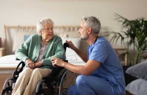 Older adults walk indoors together while another resident performs seated exercises nearby.